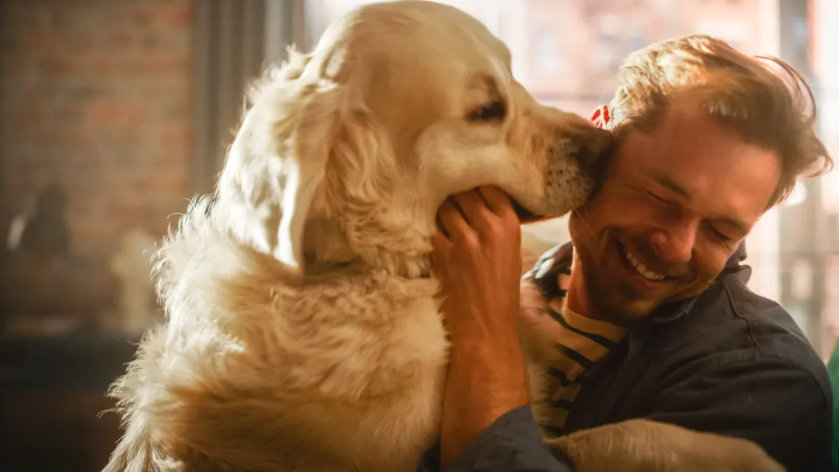 Smiling man embracing his golden retriever as the dog affectionately nuzzles his face.