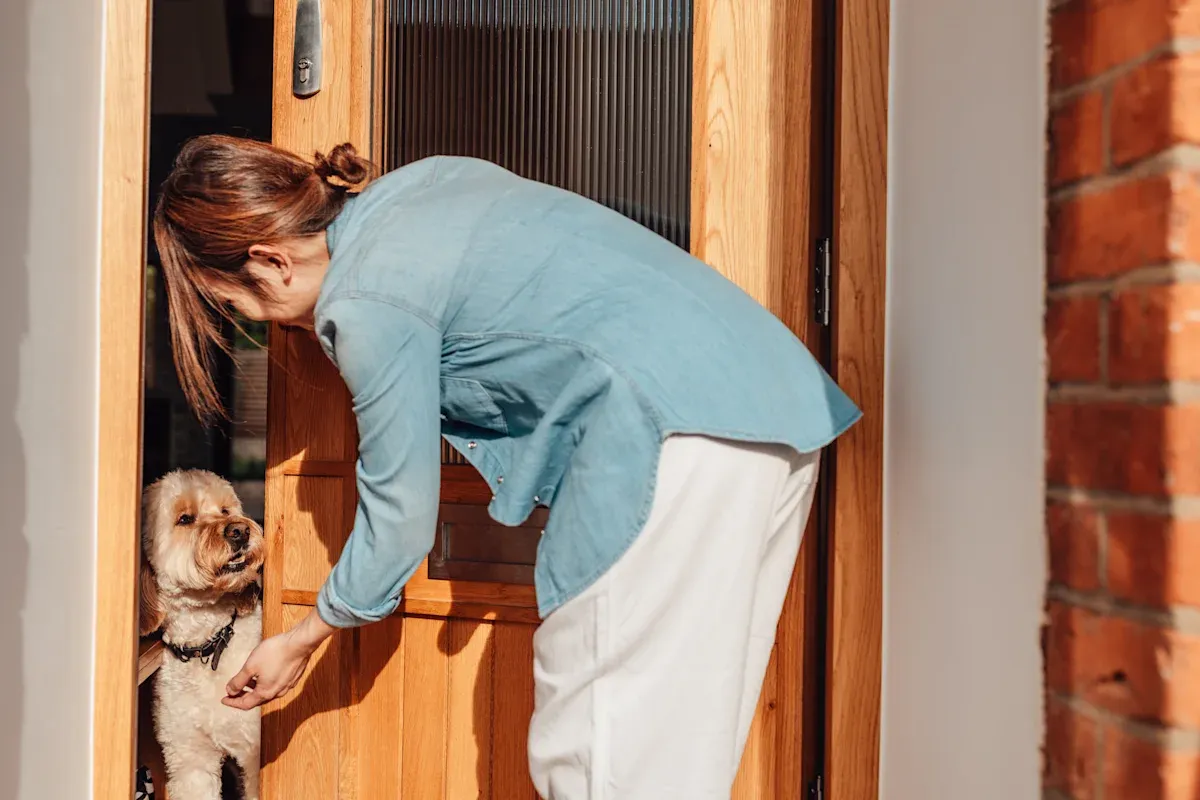A woman crouching in a doorway to greet her small dog as she arrives home.